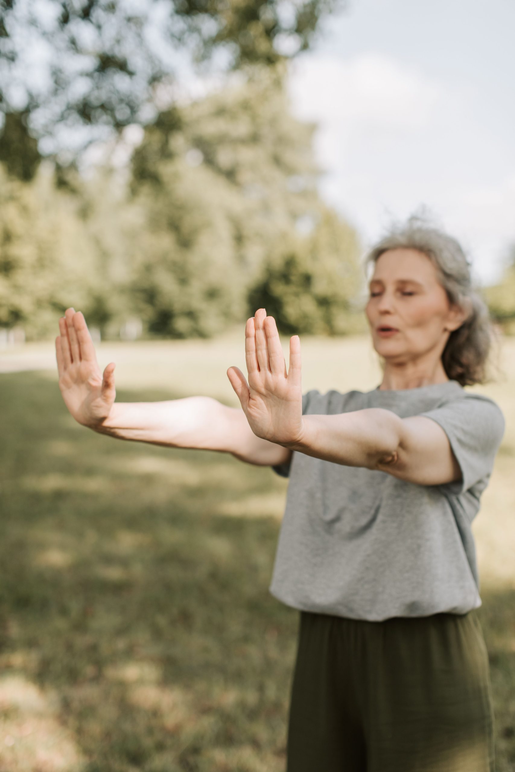 Senior woman practicing Tai Chi in a sunny park, focusing on mindfulness and healthy lifestyle.